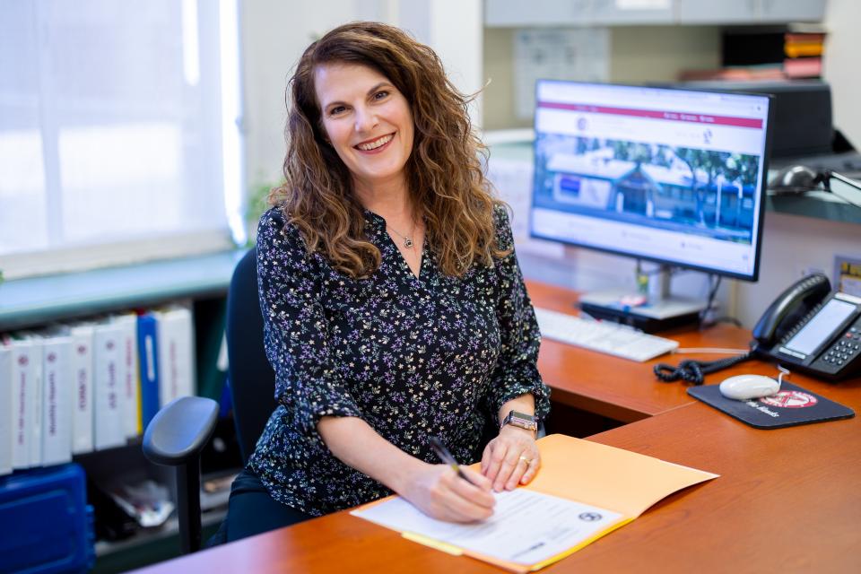 Administrative staff sitting at desk in front of an open folder, smiling and holding a pen.