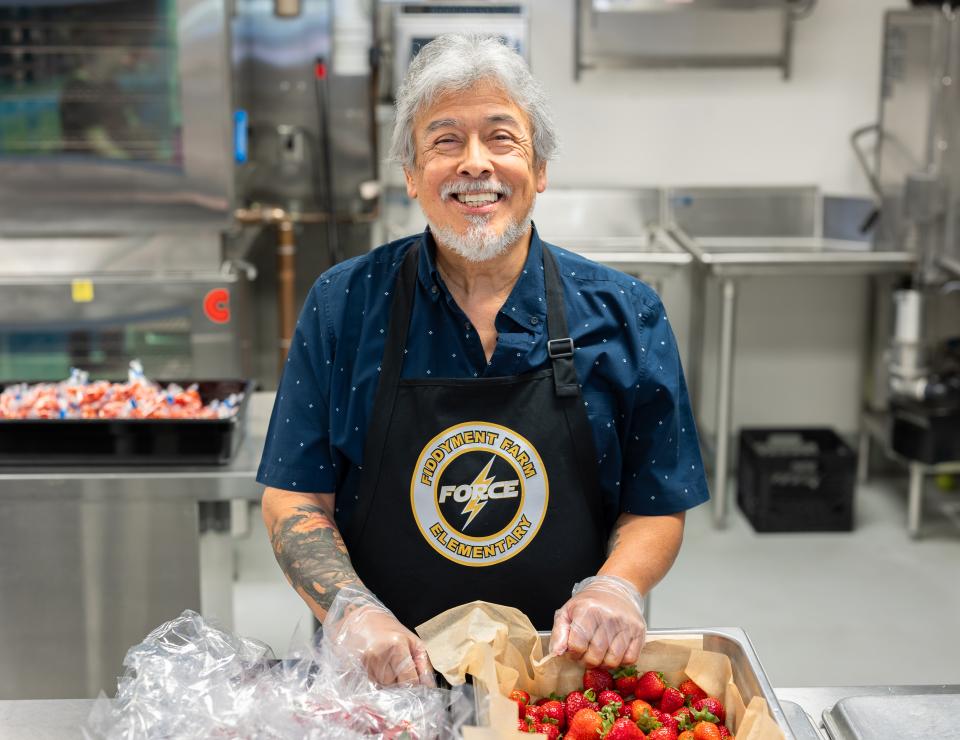 Cafeteria staff standing in school kitchen, smiling in front of a tray of strawberries. 